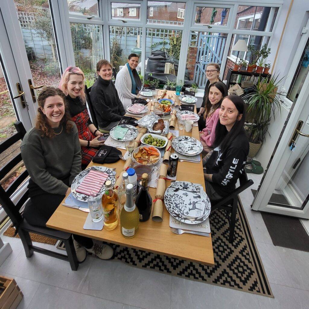 Tiny Paws MCR volunteers sitting around the table with a spread of food and Christmas crackers